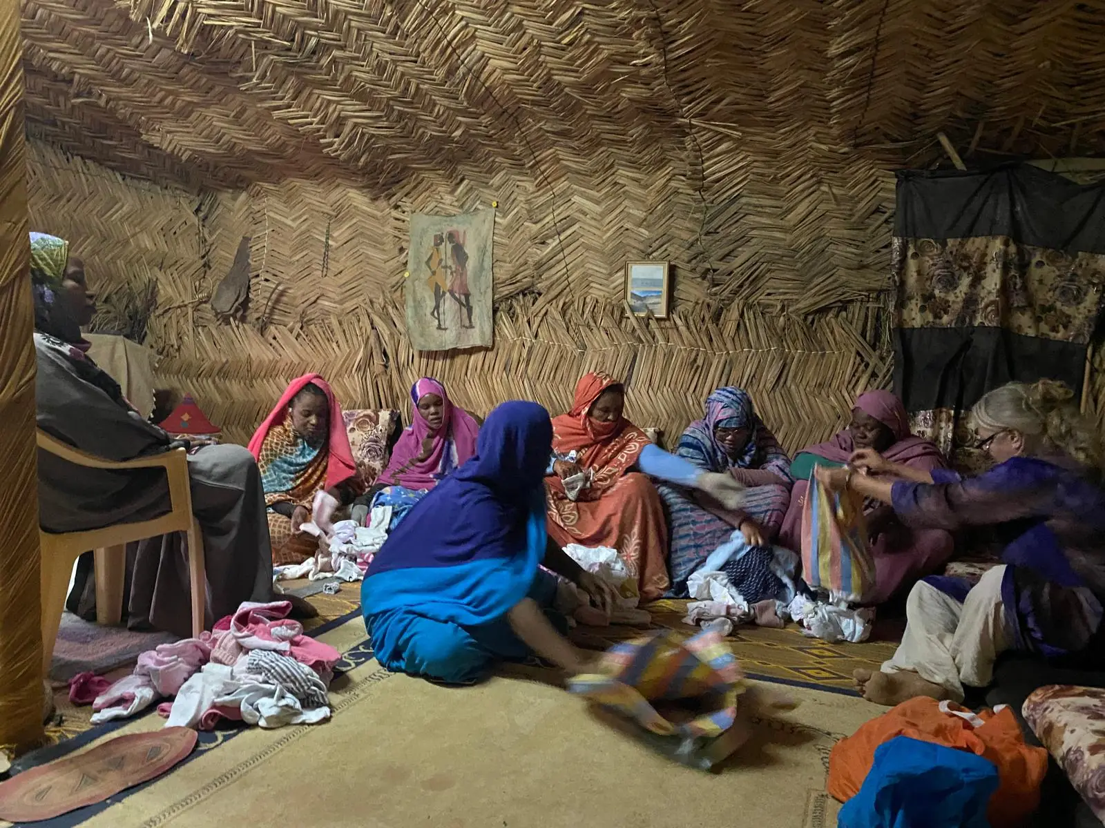 Donne sedute in una tenda di paglia che si dividono i vestiti con Barbara